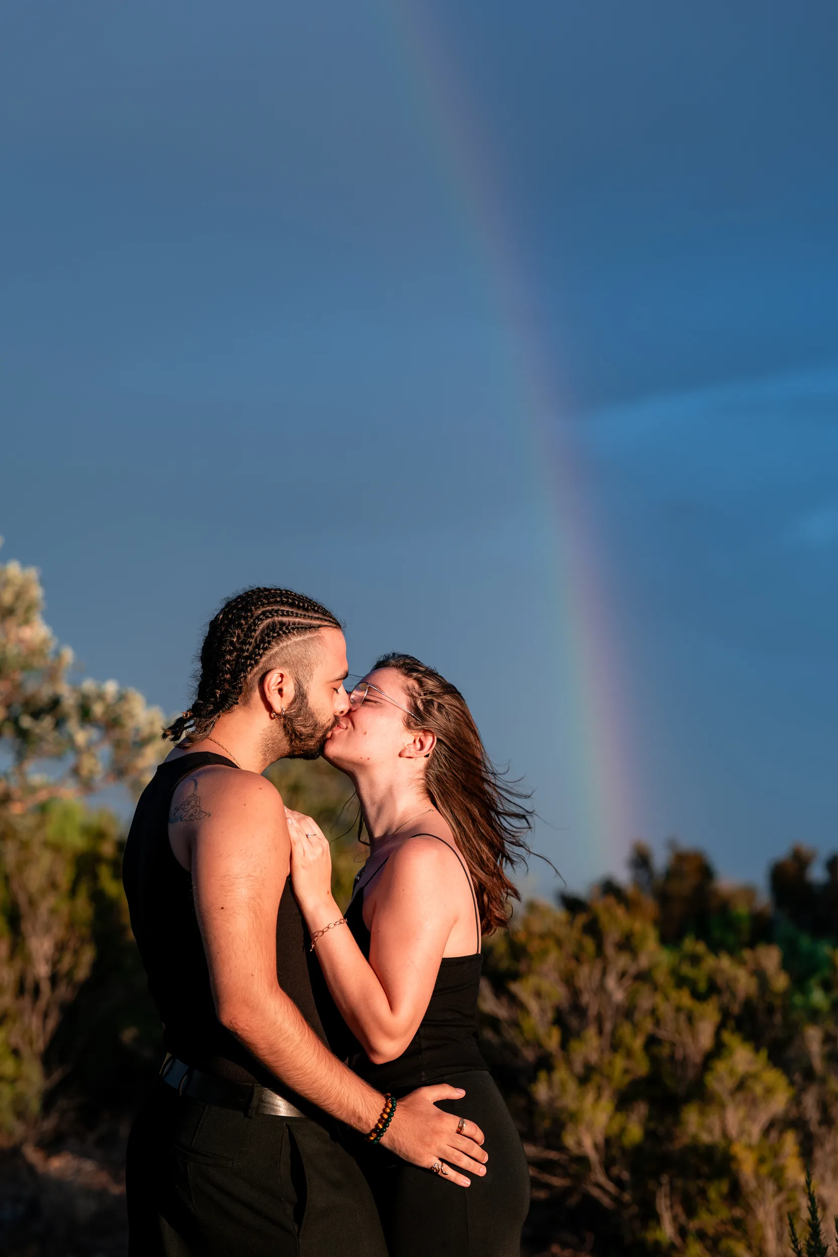 Couple s’embrassant devant un ciel traversé par un arc-en-ciel à Cap Garonne