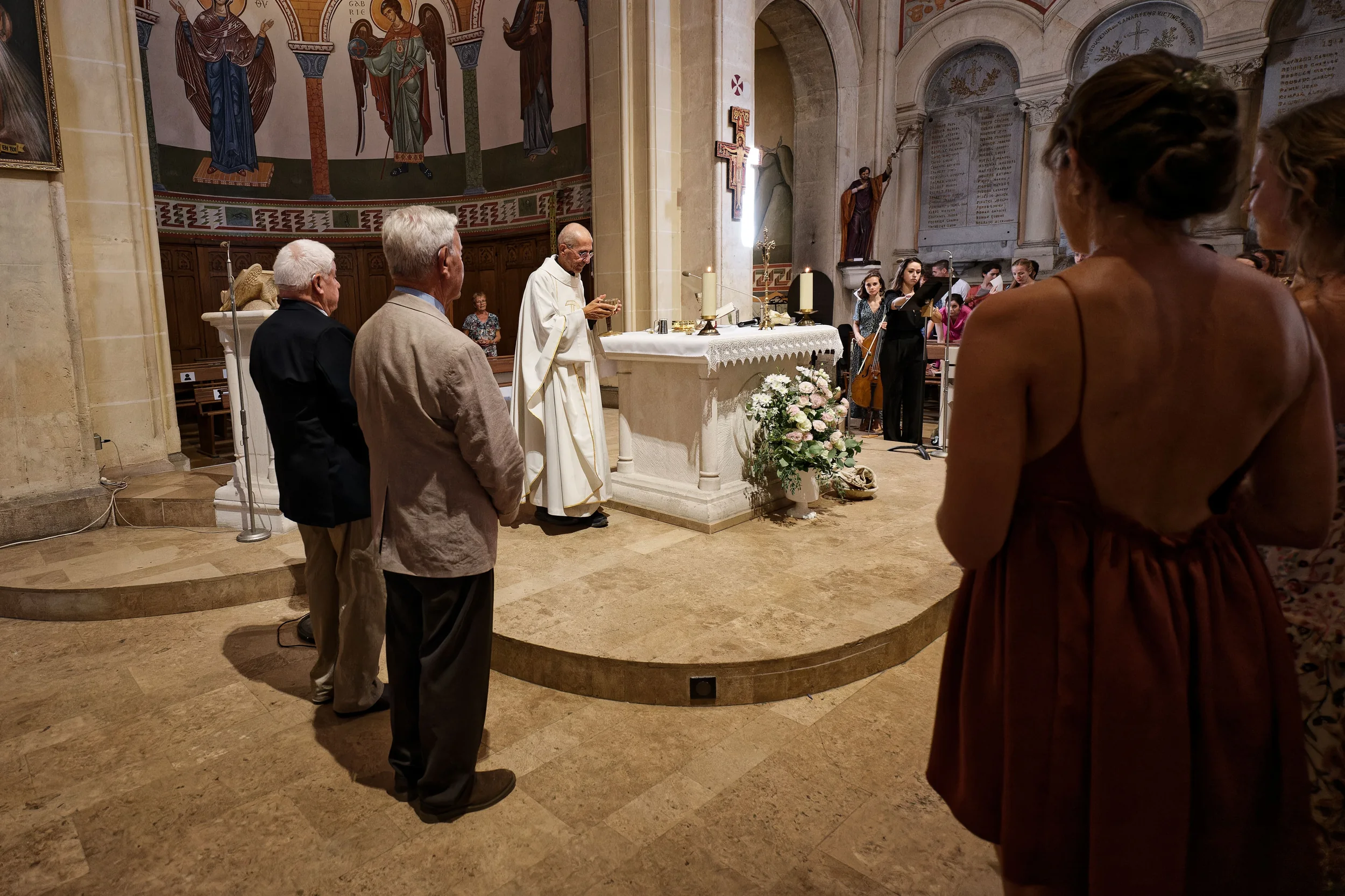 Le prêtre près de l’autel en pierre, devant les fresques du chœur, avec les proches et les musiciens autour de lui.