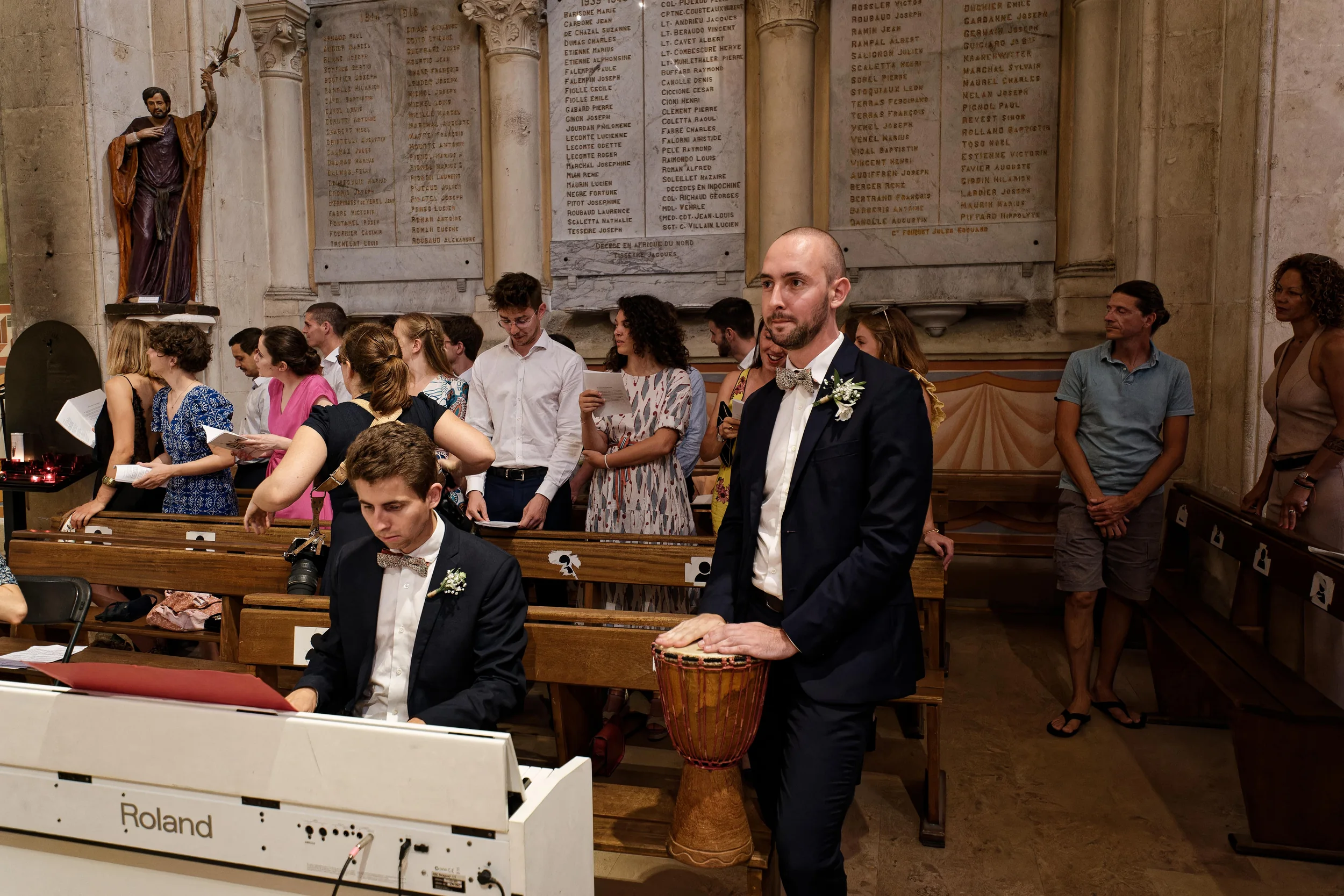 Un pianiste et un percussionniste accompagnent la cérémonie, devant les invités debout dans les bancs de l’église.