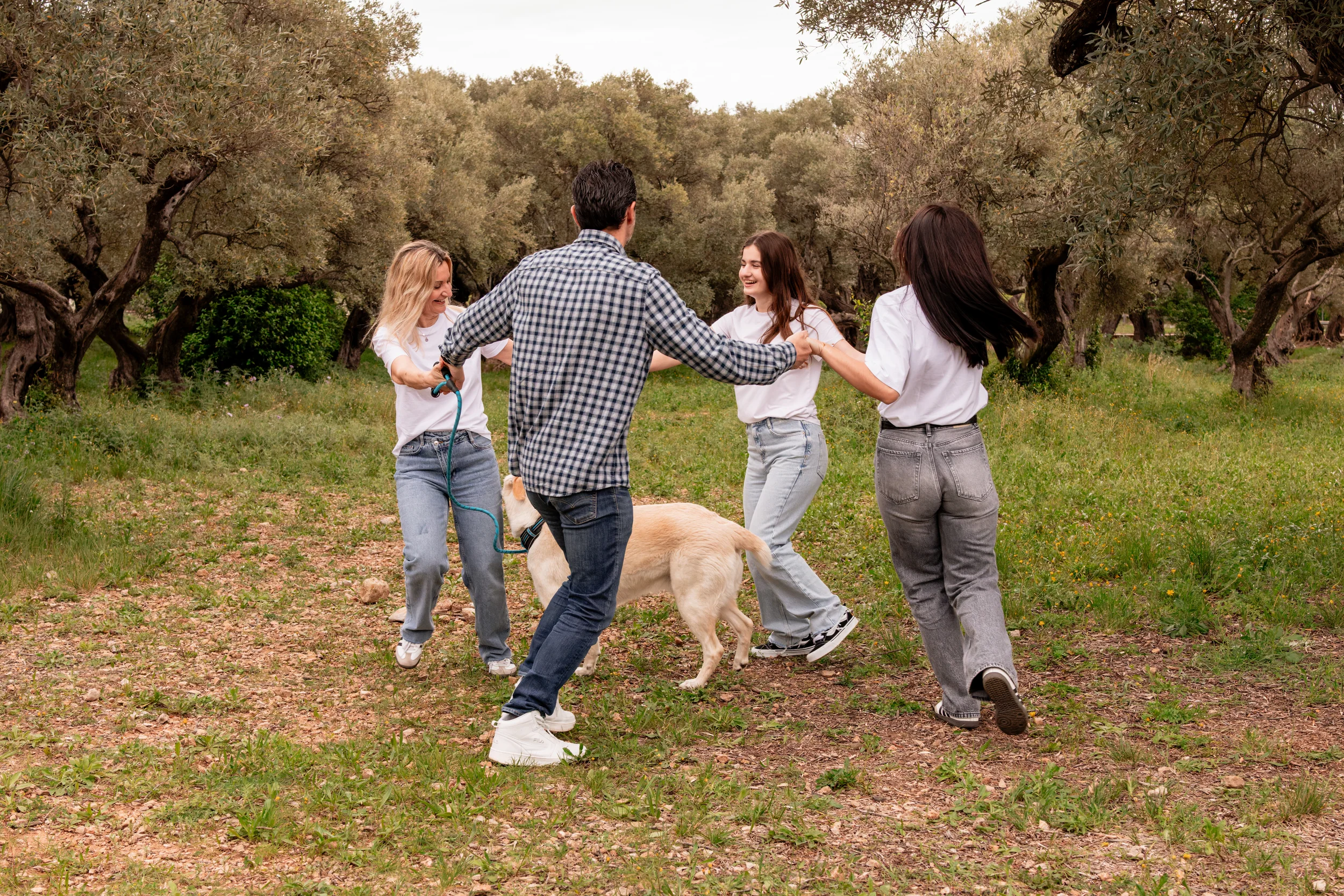 Famille qui joue en cercle avec son chien dans une oliveraie